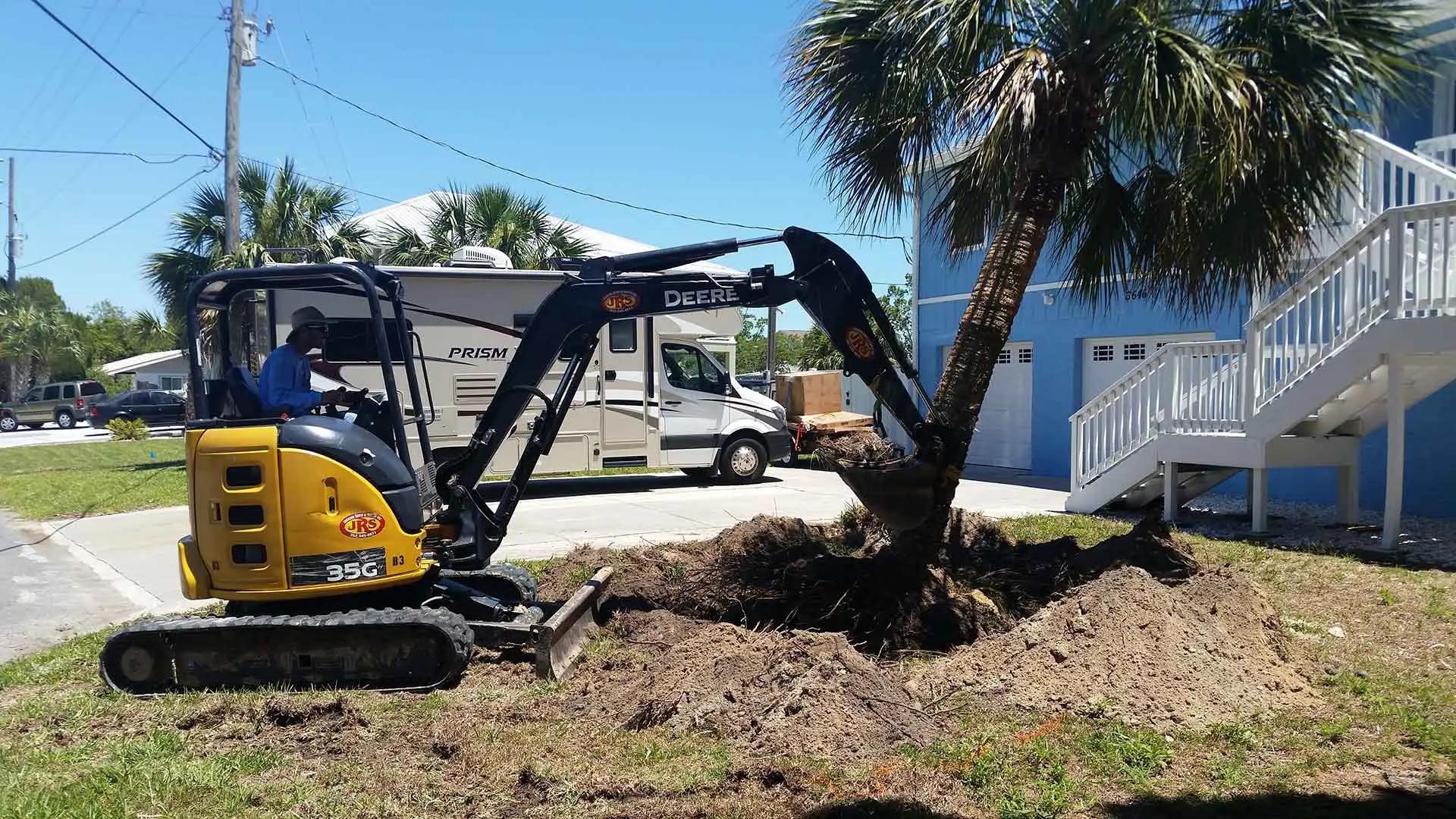 Team member using heavy machinery to knock over a small tree that will be replaced.